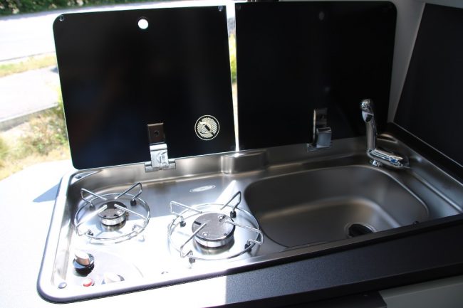 Auf dem zweiflammigen Gasherd mit Elektrozündung lassen sich so allerhand regionale Köstlichkeiten zubereiten - die Abdeckung und der klappbare Wasserhahn schaffen zusätzliche Arbeitsfläche.